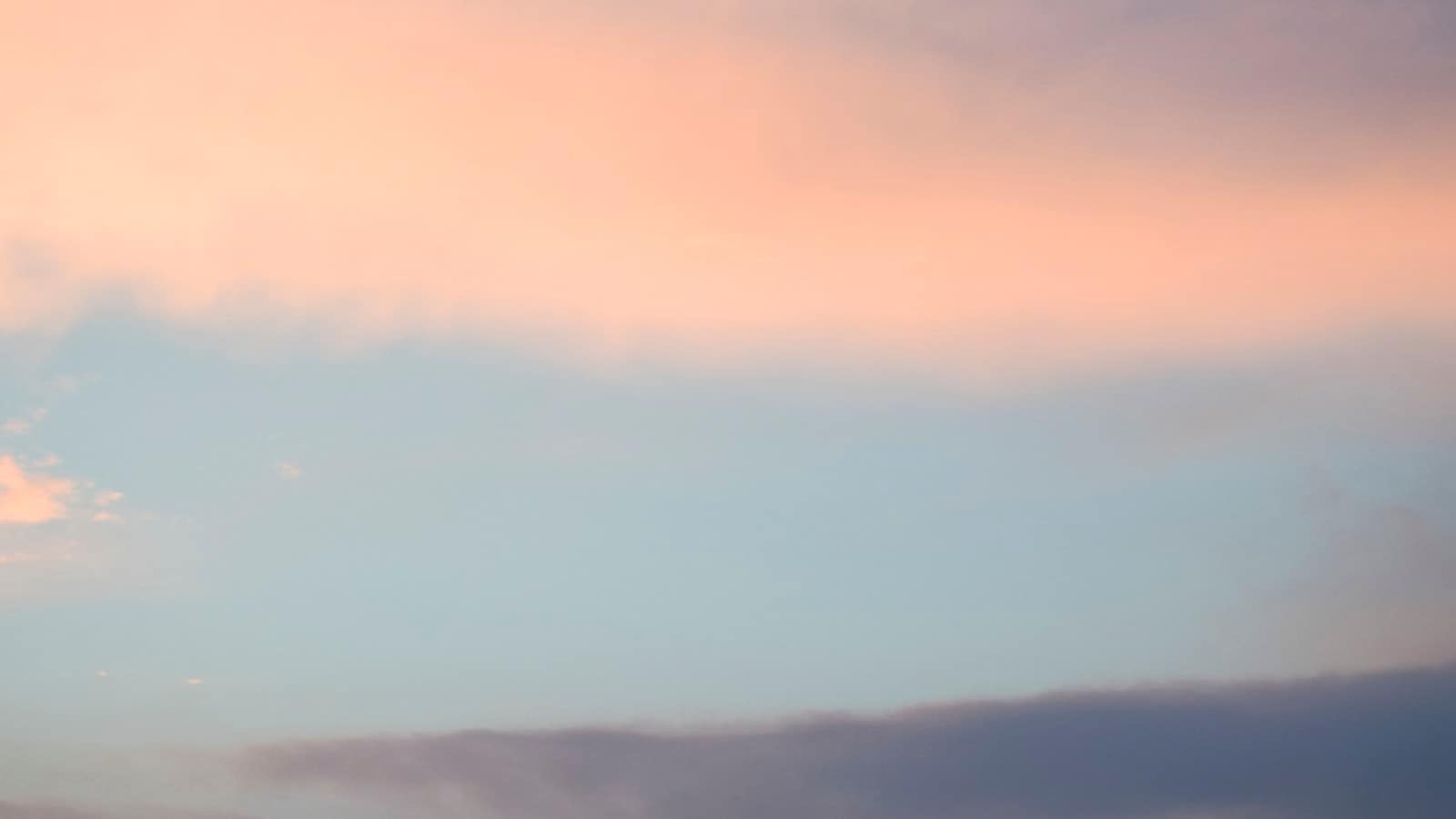 A soft pink and lavender sky over calm water at dusk
