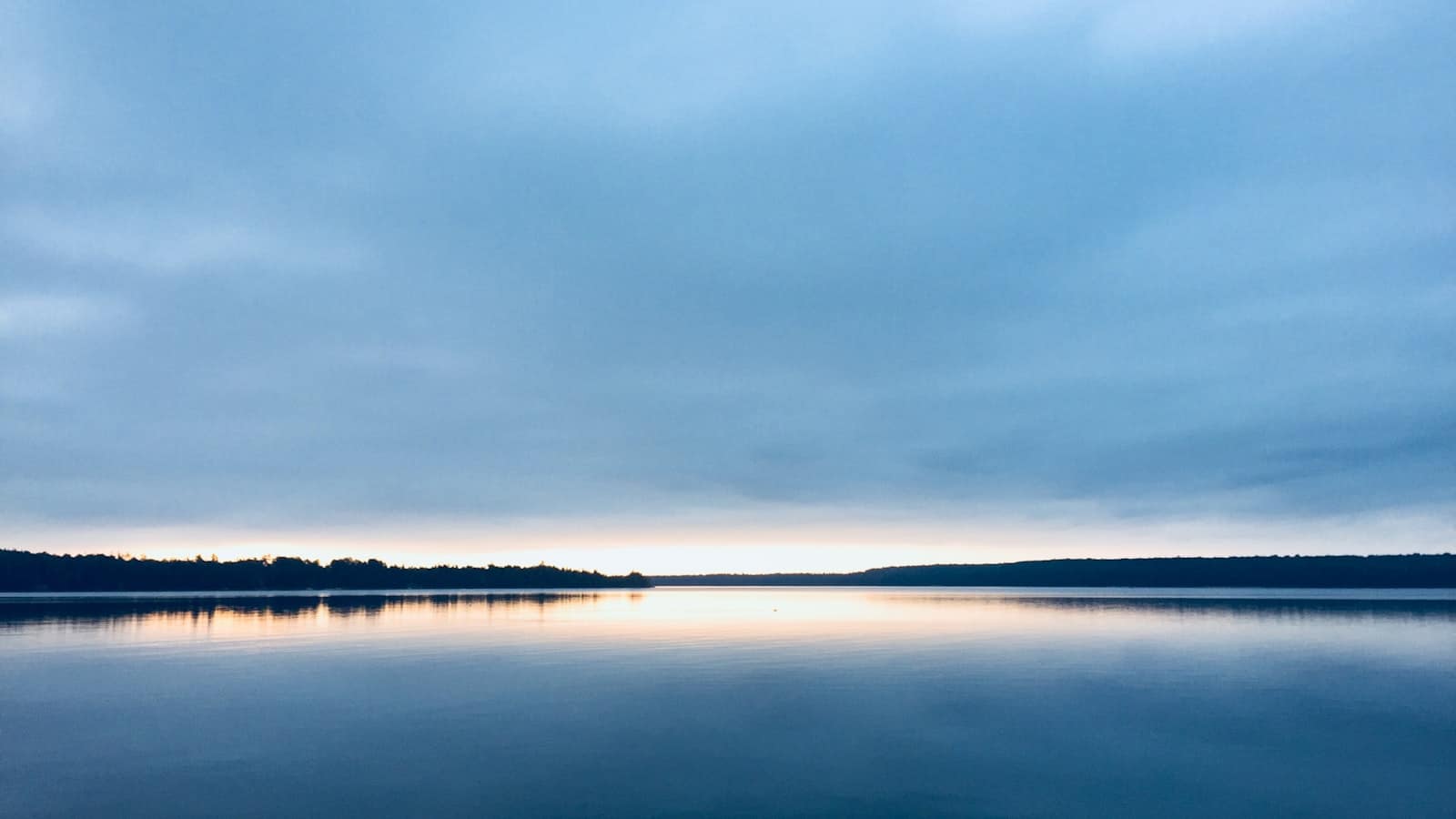 A still lake at dawn reflecting a calm, open sky