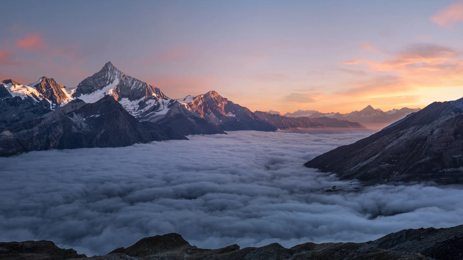 Snow-covered peaks catching the last of the sunset above a still sea of cloud